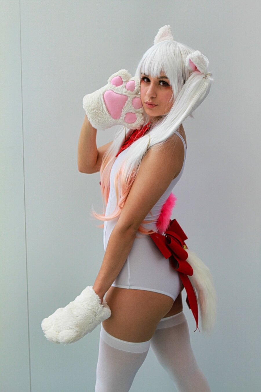 Person wearing cat cosplay.  She has white shorts, white stockings, white paw gloves with pink beans and white ears.  She's looking back over her shoulder at the camera.