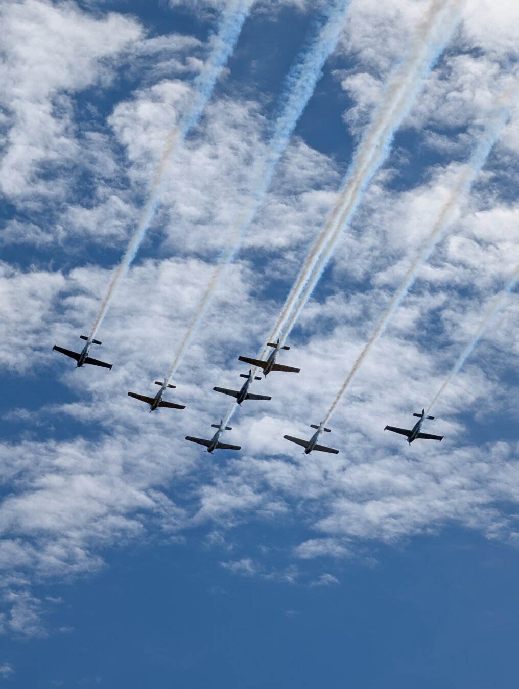 Seven Beechcraft T-34 Mentor airplanes flying in formation with clouds in the background.  The planes are operated by the Veteran Airlift Command Tribute Wing (if I remember correctly).