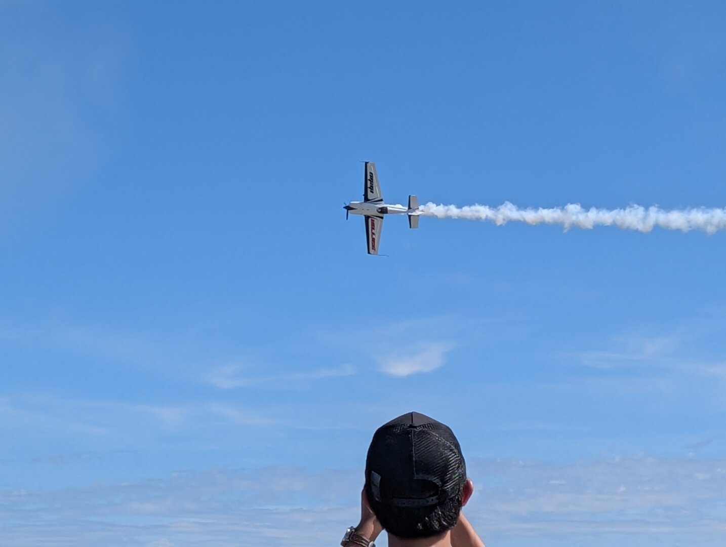 An Extra 330SC airplane performing an aerobatic maneuver.  The pilot is Aarron Deliu.   A man taking a picture with his phone is also visible, but that's not important.