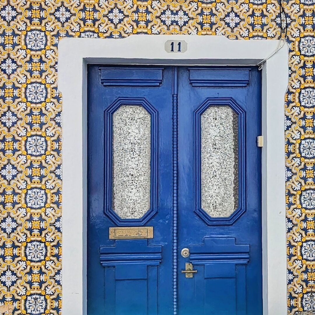 Royal blue double door numbered 11 with textured glass panels, framed by an entire facade of ornate blue-and-gold Portuguese azulejo tiles in Terceira, Azores.