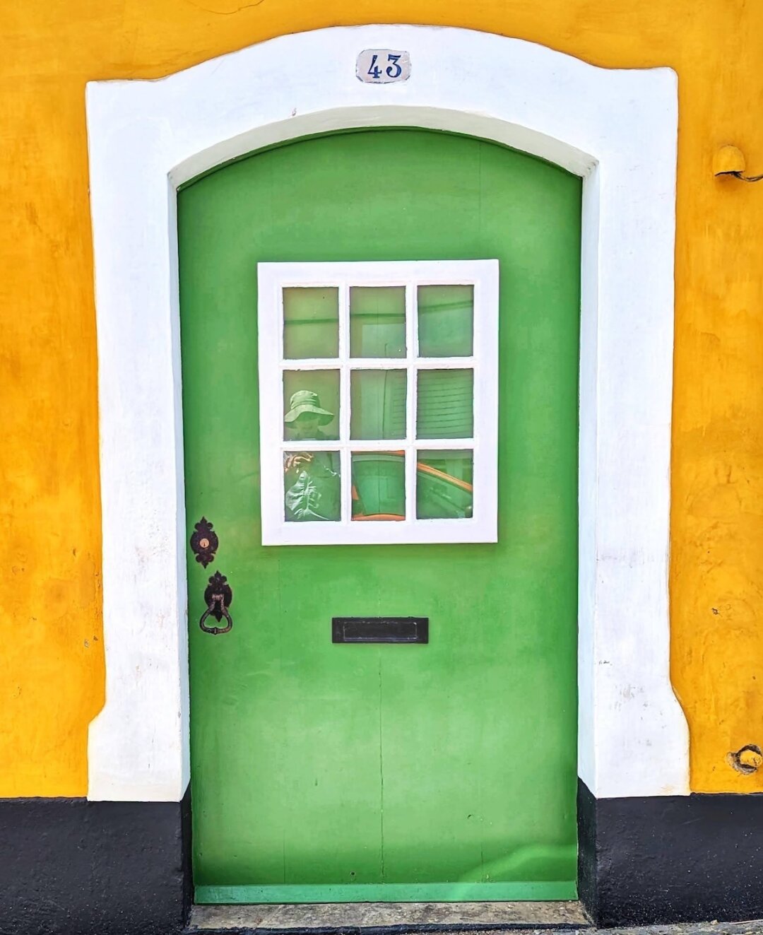 Bright green door numbered 43 with a white nine-pane window and black iron knocker, set against a mustard-yellow wall in Terceira, Azores.