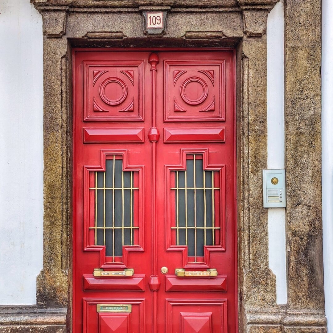 Bright red Art Deco-style double door numbered 109 with gilded iron-barred windows, set in a weathered stone surround in Terceira, Azores.