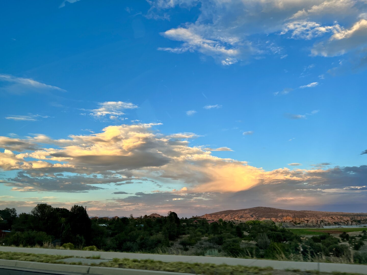 The setting sun illuminates clouds in the distance. Low mountains occupy the background, a narrow strip of highway occupies the lower part of the image.