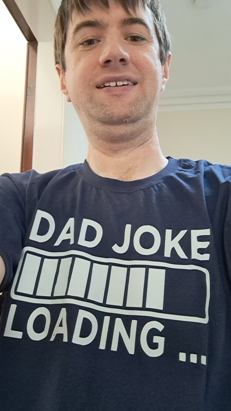 A photo of a 39 year old white man wearing a blue t-shirt that reads "Dad joke loading".