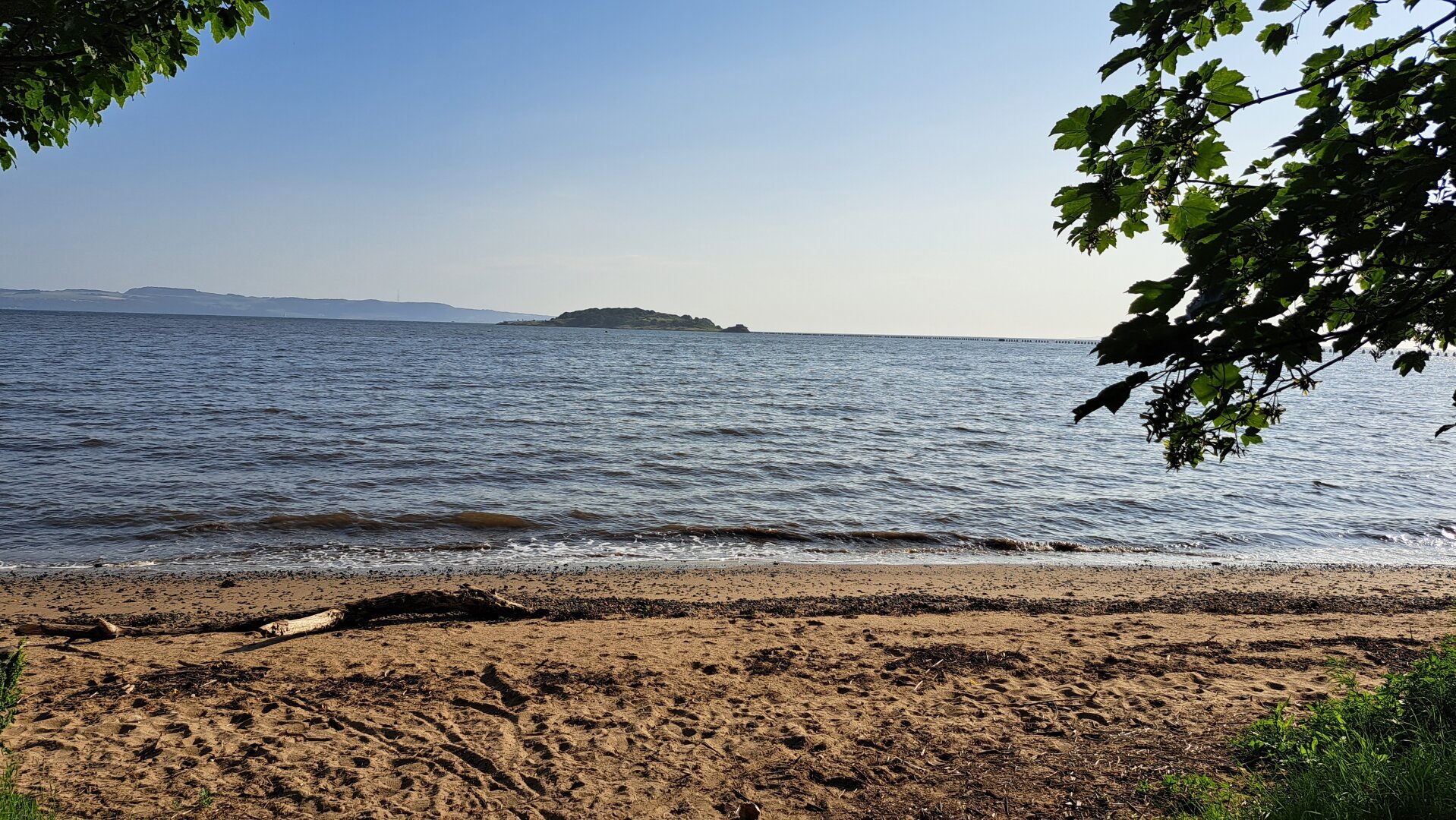 A sandy beach in the morning. Blue sky overhead and a tidal island in the distance.