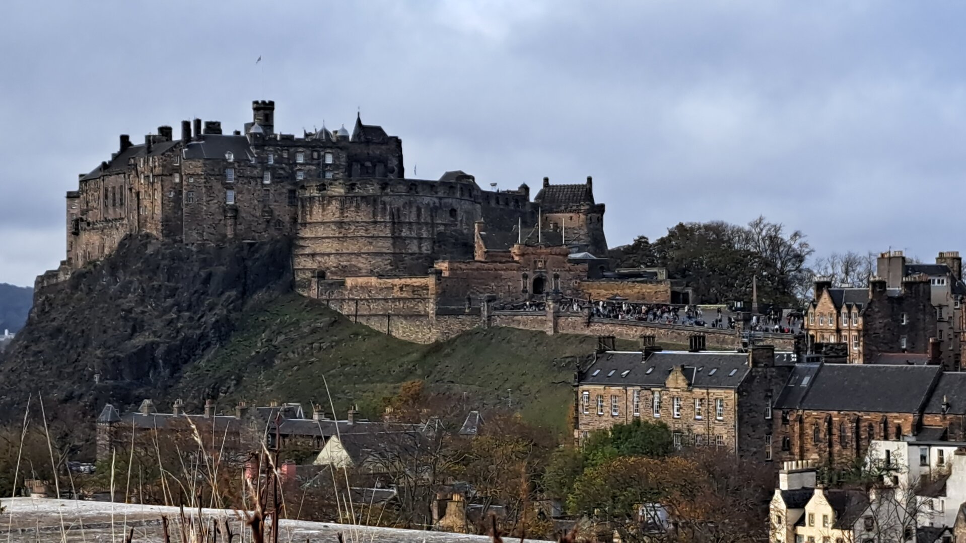 Edinburgh castle looms over the city of Edinburgh on a cloudy day.