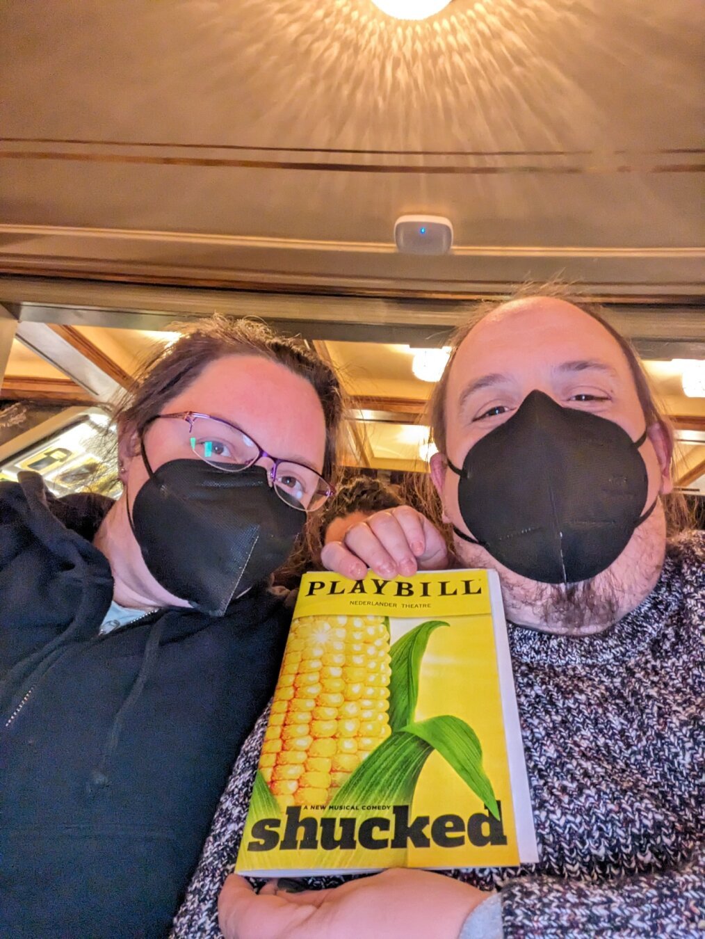 Photo of dracoling and partner wearing masks and holding up Playbill for the Broadway Musical Shucked