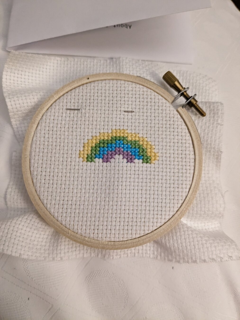 Cross-stitch in progress showing a rainbow with yellow, green, blue and purple stripes.