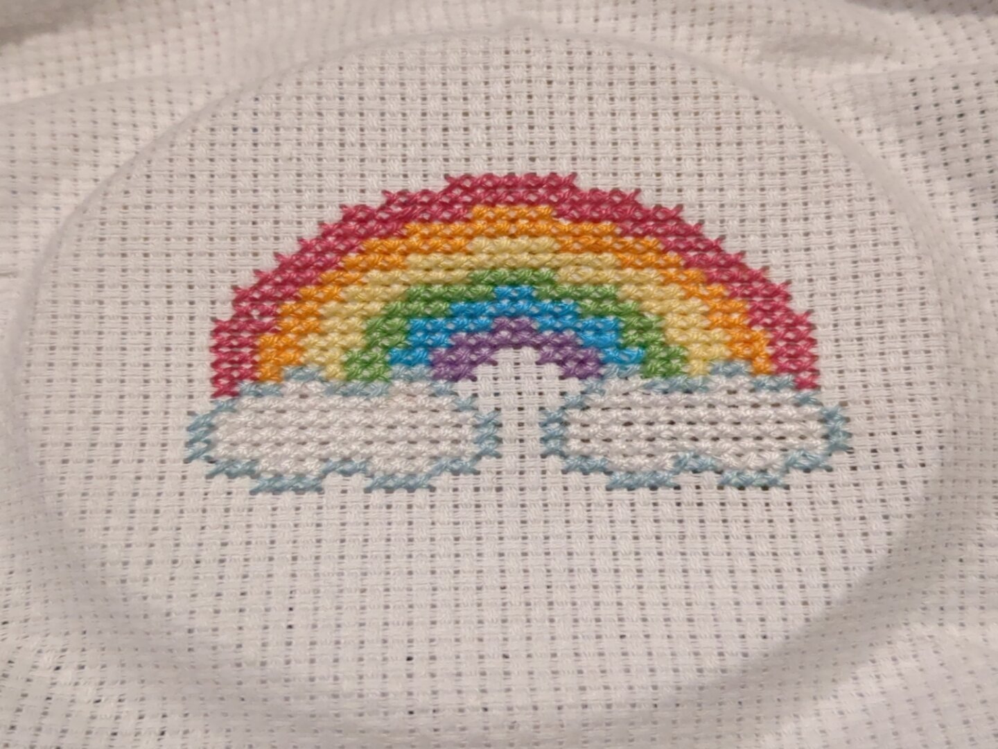 Cross stitch canvas showing a rainbow with clouds on both ends.
