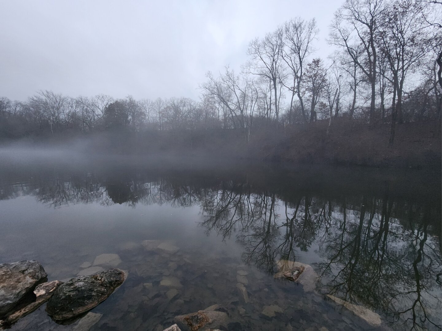 Reflections on a pond in fog with rocks in the foreground