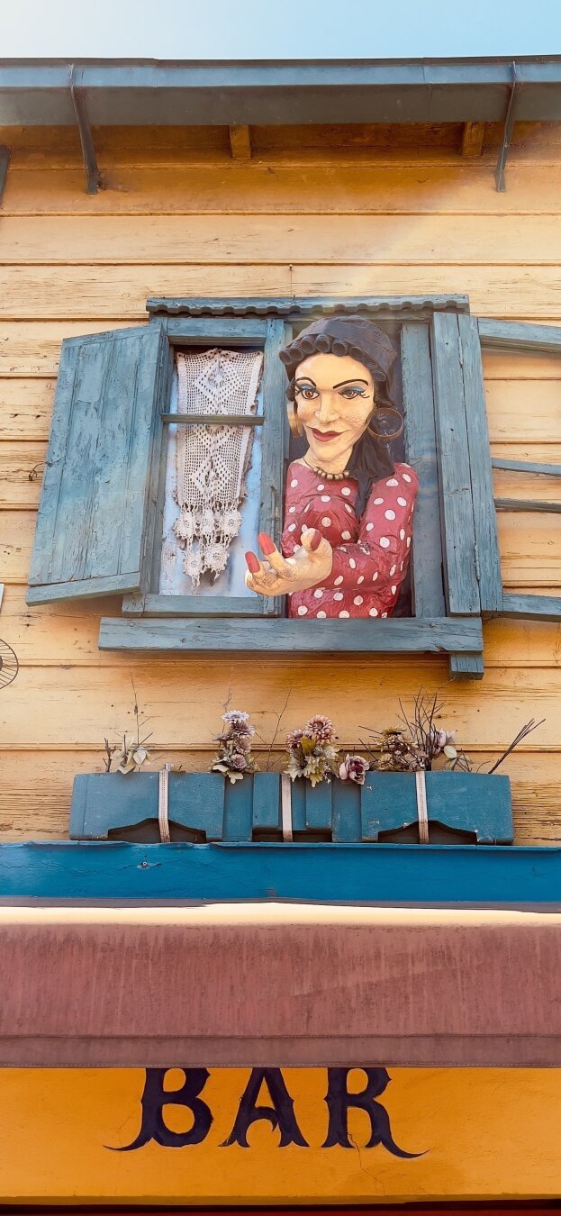 Woman in a window is tending her hand. She seems to say « come in »!