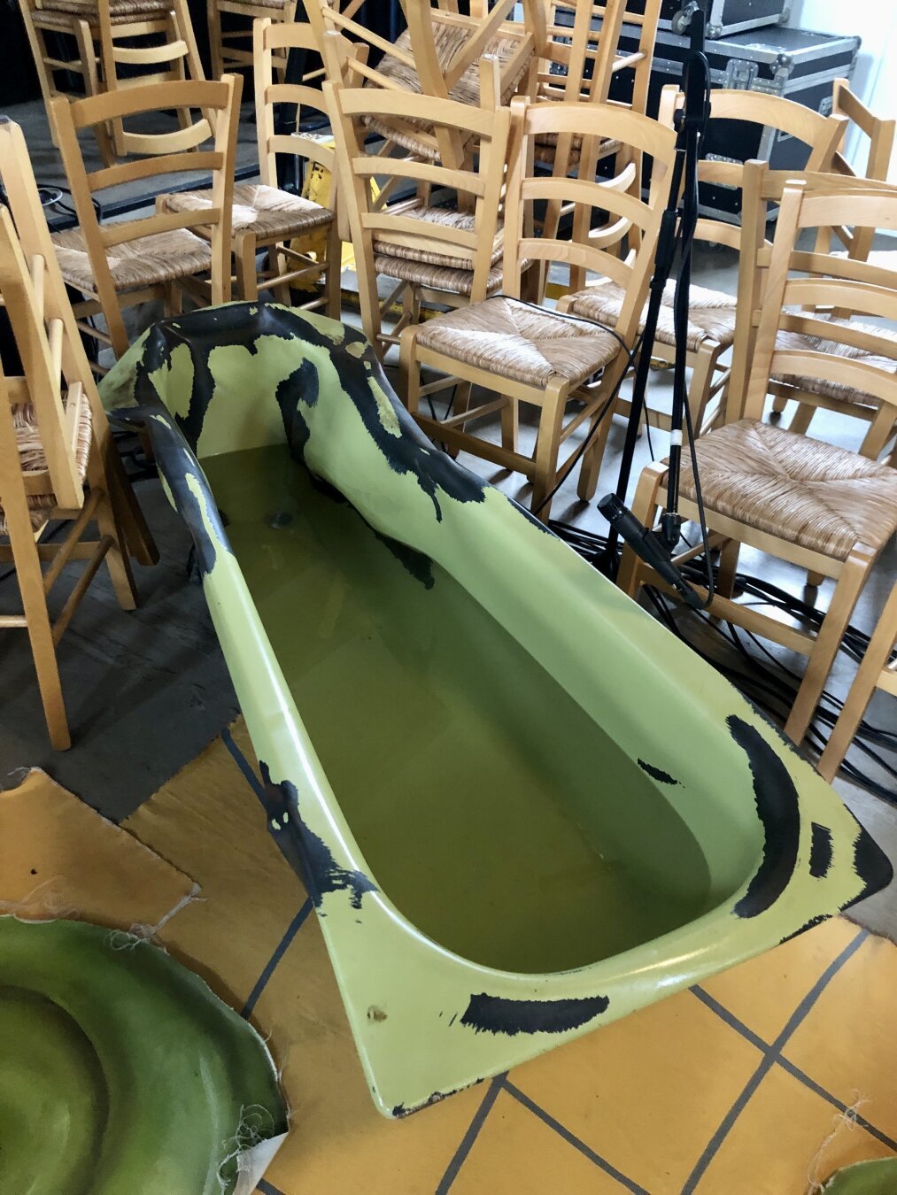 Green, squished bathtub squeezed in between a lot of chairs.