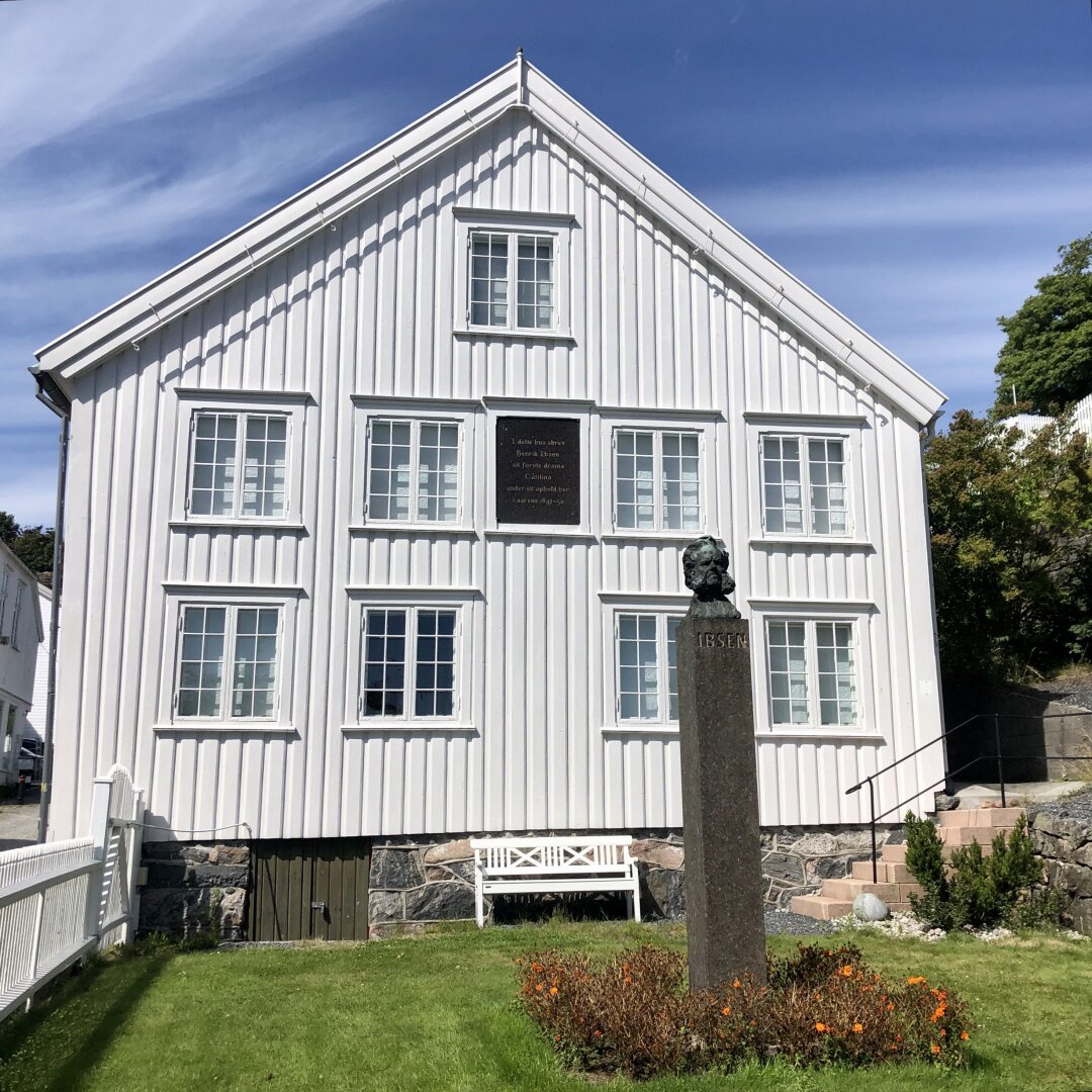 Small statue of Henrik Ibsen outside a white wooden house where he used to work as an apothecary.