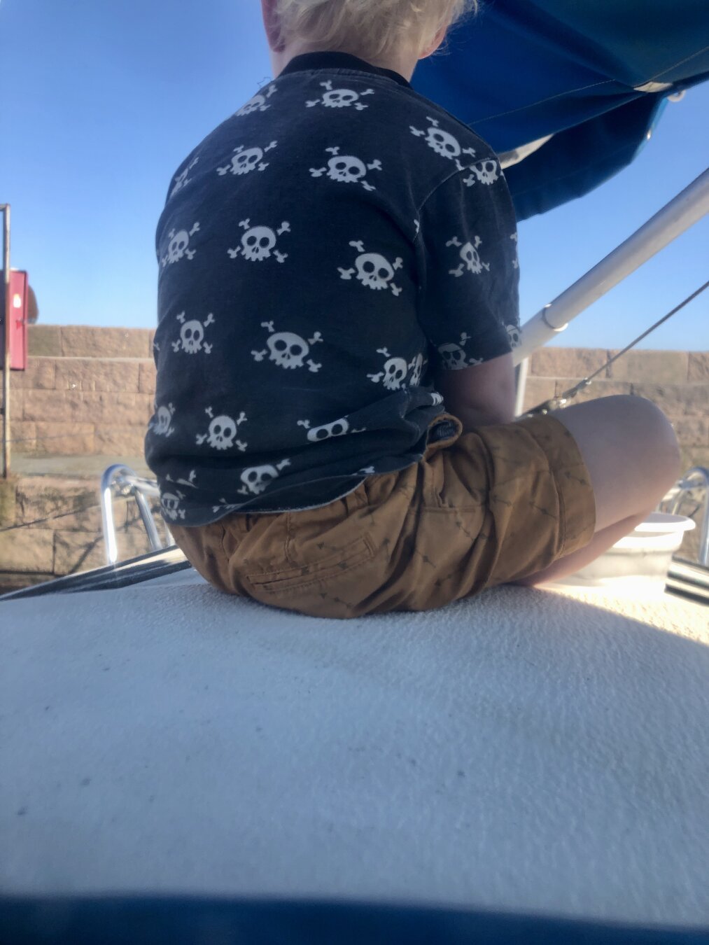 Small child in a pirate T-short sitting on deck on a sailboat.