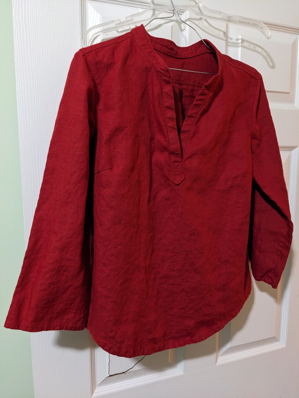 A red linen tunic is hanging in front of a door
