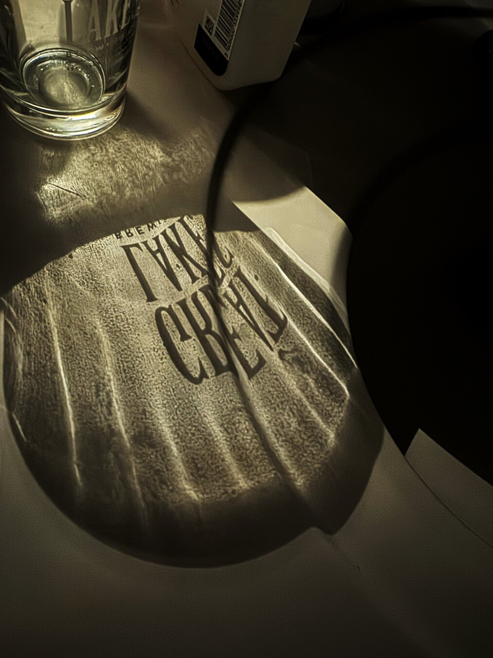 A small glass casts shadows on a countertop.  You can almost make out the words in the shadows. (Spoiler alert: it says Great Lakes - it’s a small pint glass from Great Lakes Brewing in Cleveland, Ohio. Only the alt text readers get that info.)