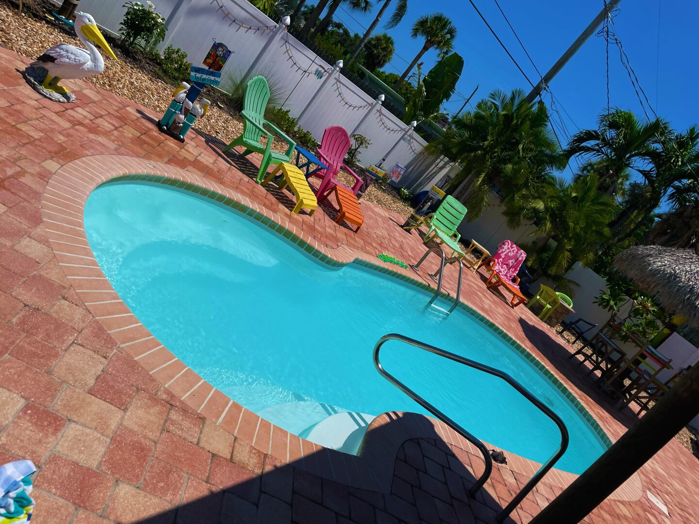 There’s a pool with blue water. Surrounding the pool is a red stone patio. In the upper left a pelican statue looks serenely over the tableau. There are a few different Adirondack chairs baking in the sun. It’s probably 100 degrees but that’s hard to tell via the photo. Florida is not the photographer’s favorite destination but family are here so…