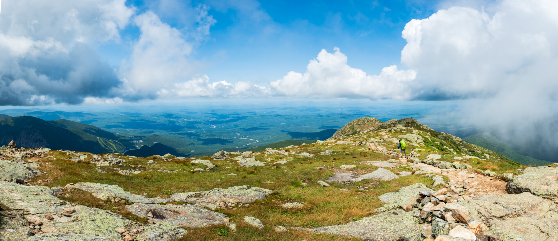 A panorama looking north from the summit of Mt Lafayette with a an Appalachian Trail through hiker heading north. Puffy clouds fill the sky with an alpine view below.
© Tom Goetz. All rights reserved. Training an AI on this image is expressly forbidden.