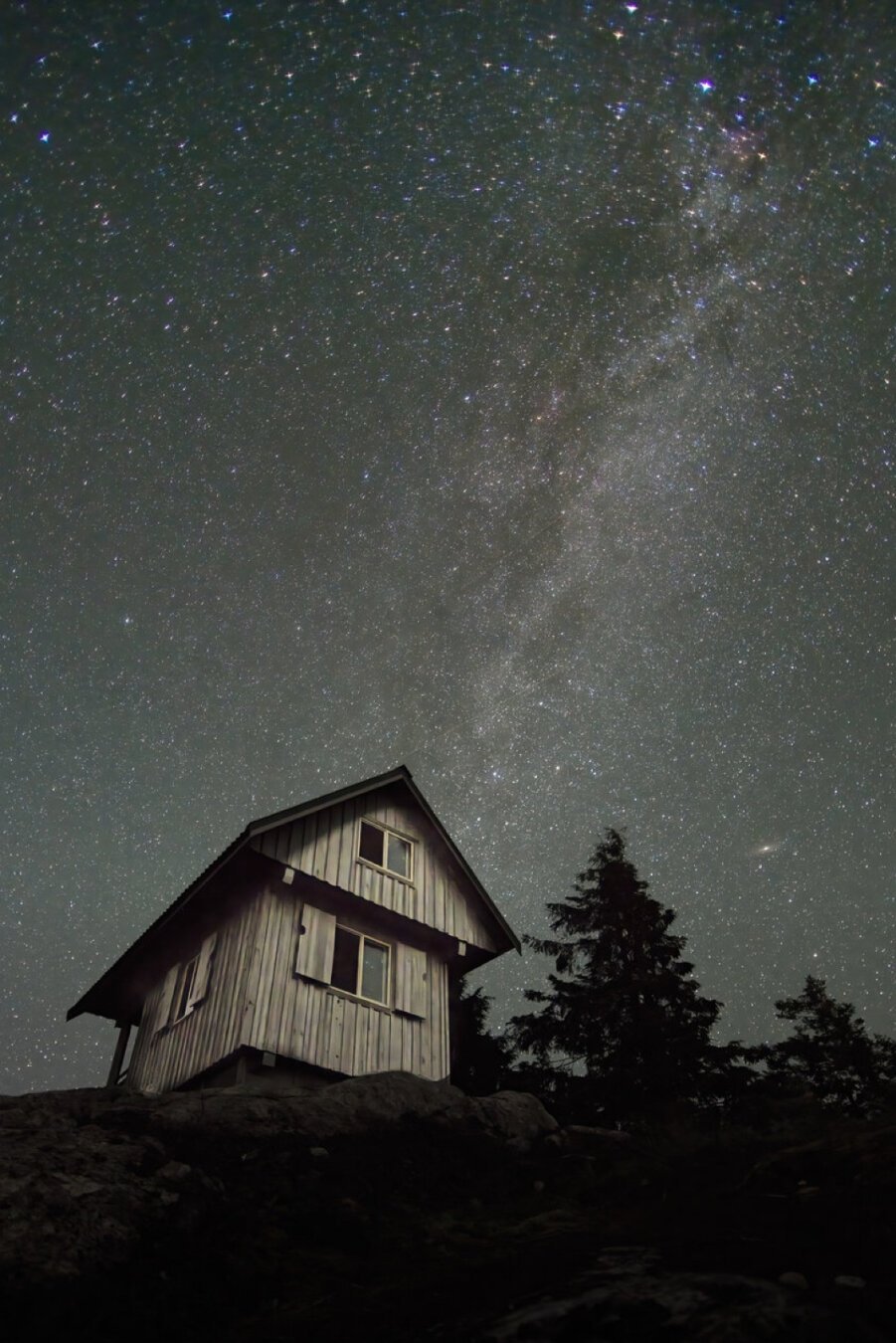 A mountain cabin at night with stars and part of the milky way above