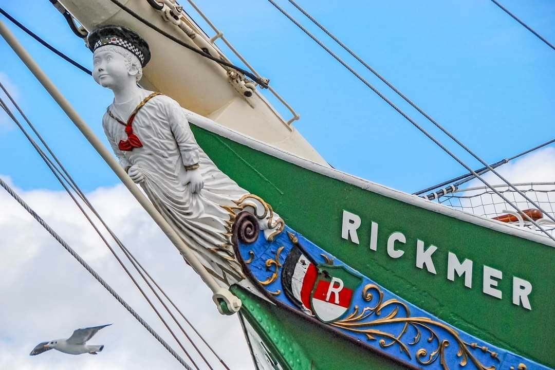 Prow of an old sailing ship with a figurehead. A flying seagull can be seen in the background.