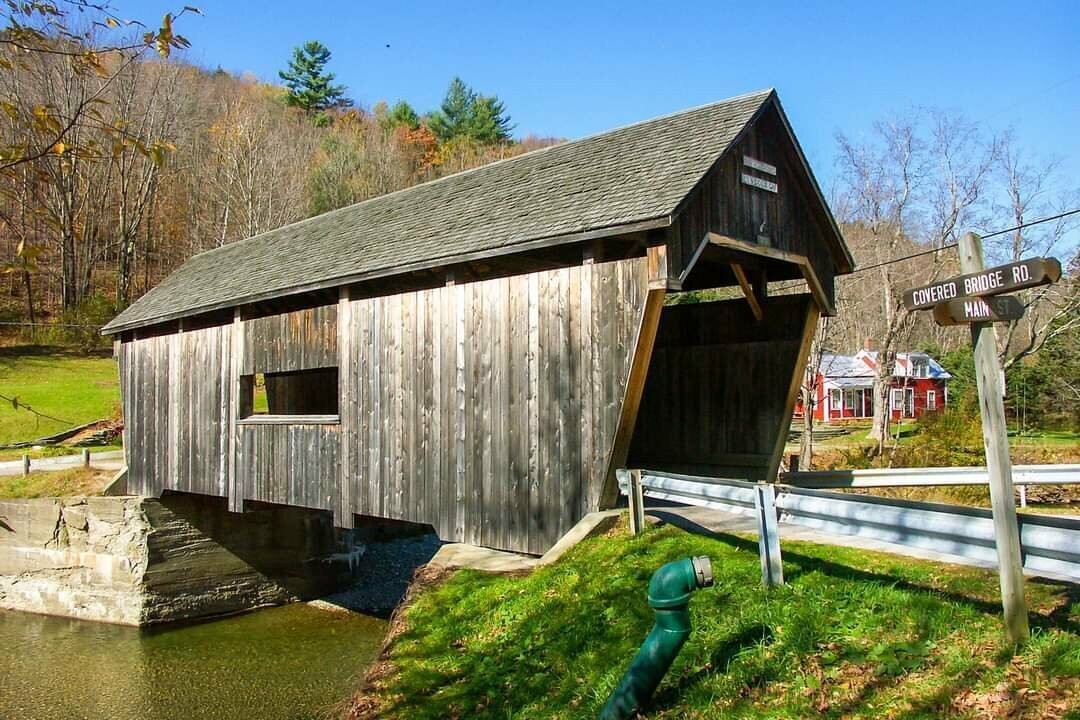 Old wooden covered bridge over a small river, open to traffic.