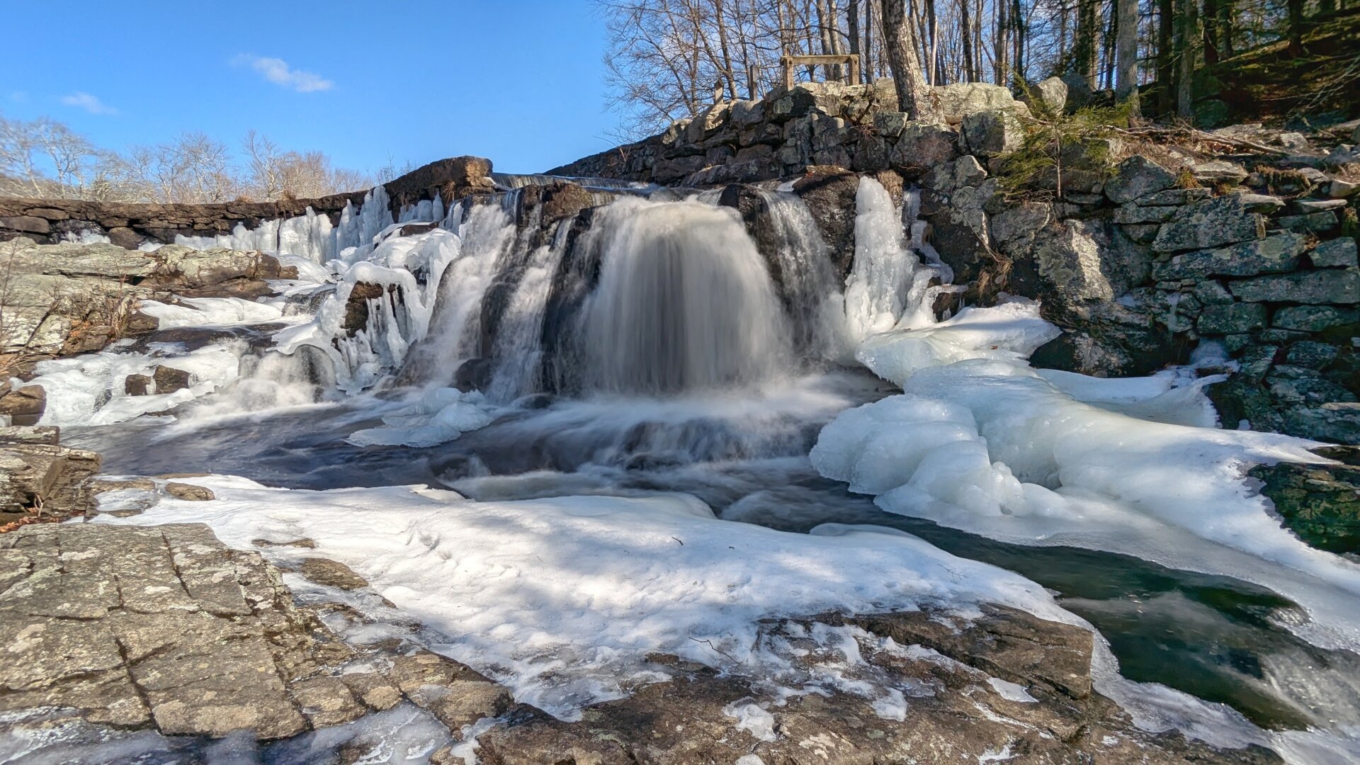 A partially frozen waterfall under a bright blue sky.