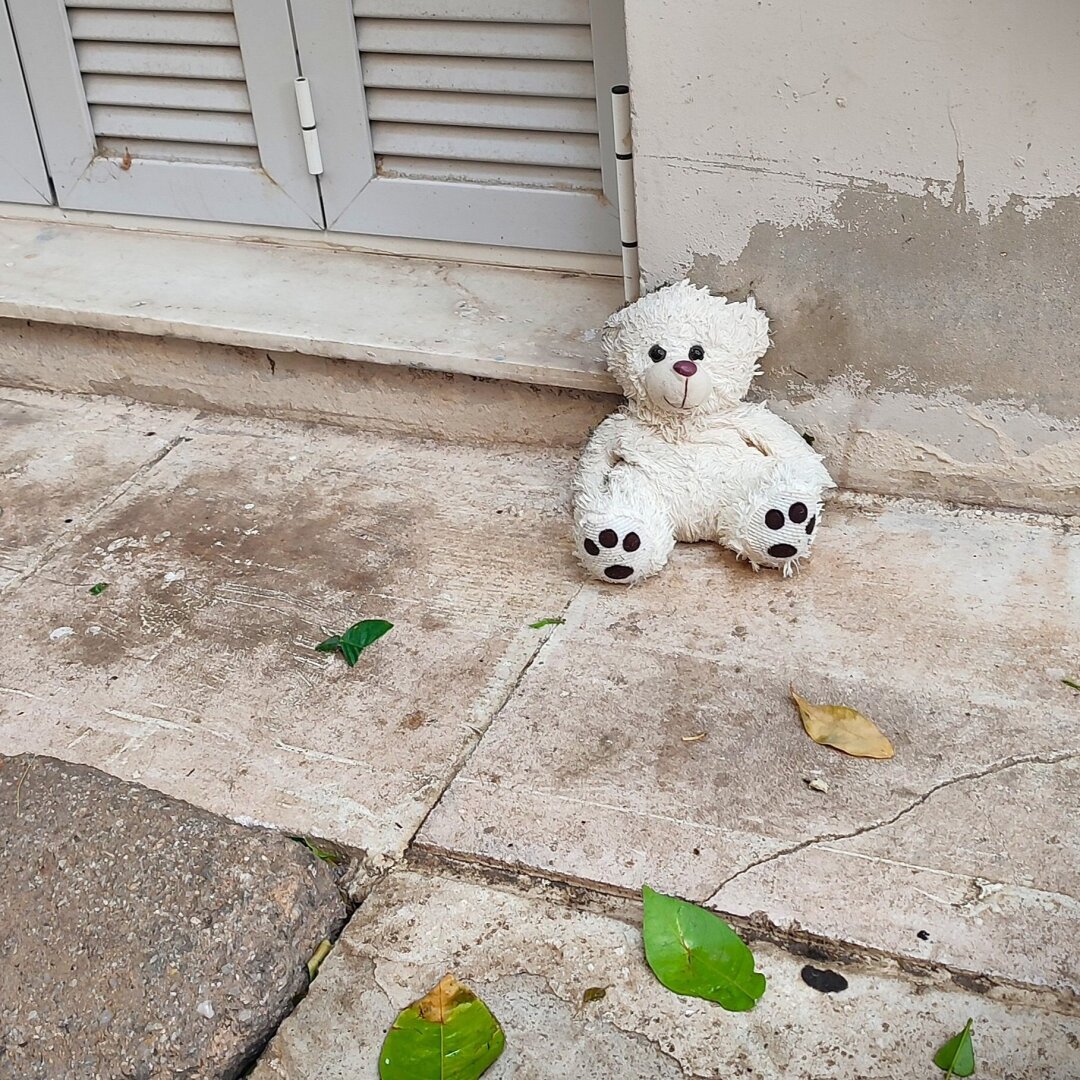 A teddy bear left leaning against the wall on the sidewalk.