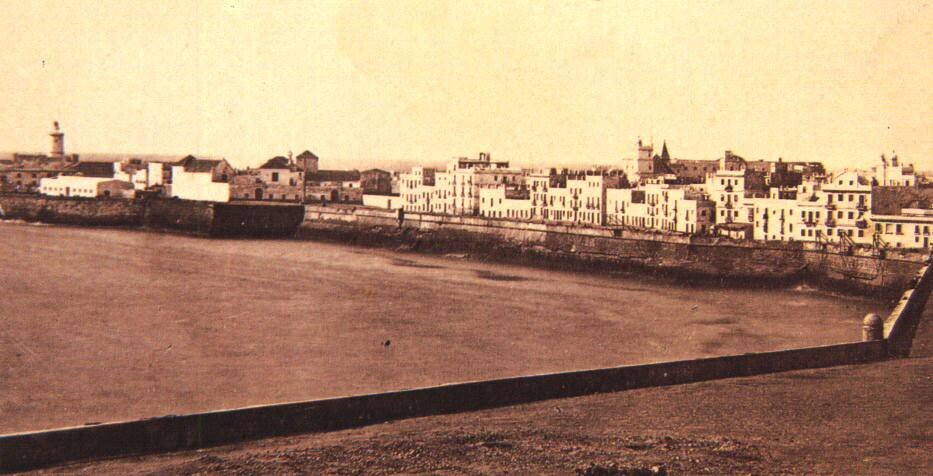 Vista de la muralla con una fila de casas blancas de 2 a tres planas y el faro al final.