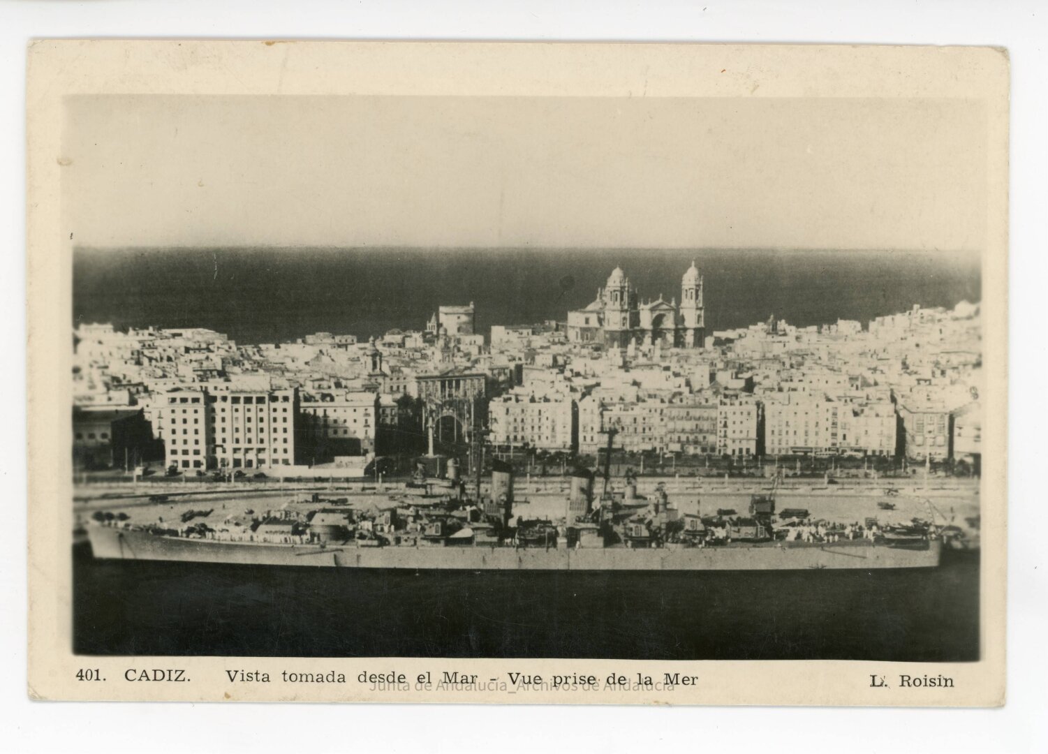 Vista desde el aire del puerto donde hay un gran acorazado. Al fondo se ve la ciudad.