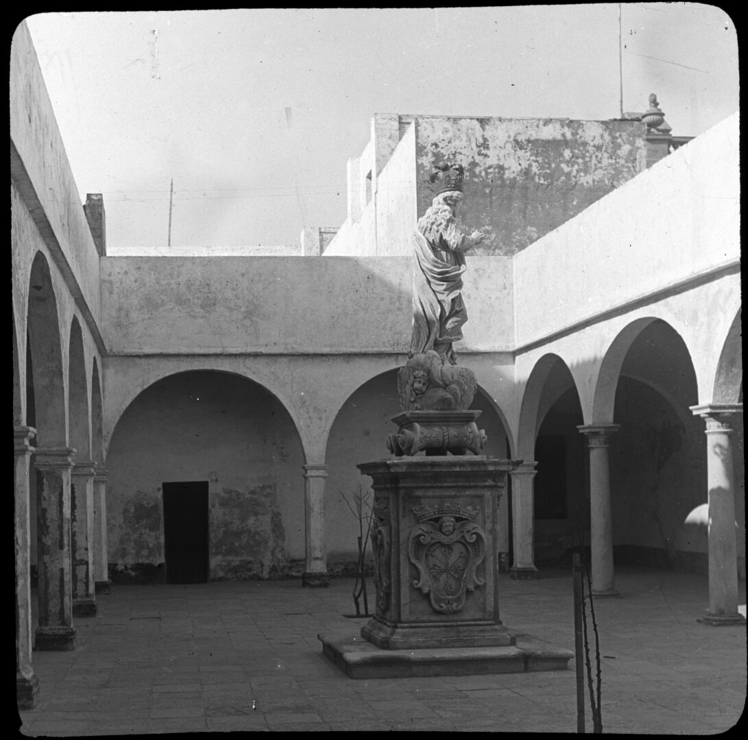 Patio abierto con arcos y una estatua sobre un pedestal.
