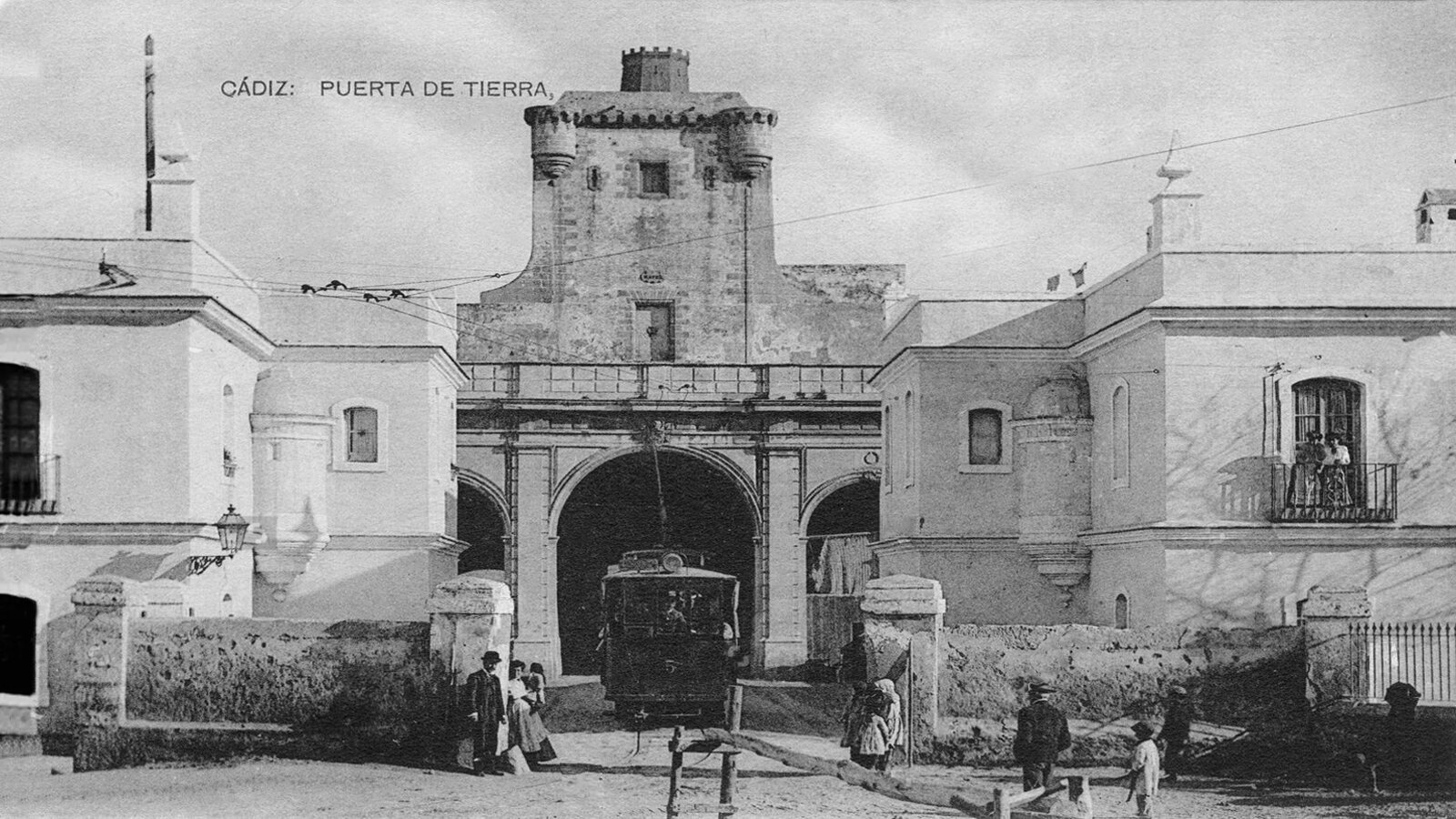 Muralla con una puerta por la que va a pasar el tranvía. A los lados hay dos edificios de dos plantas.
