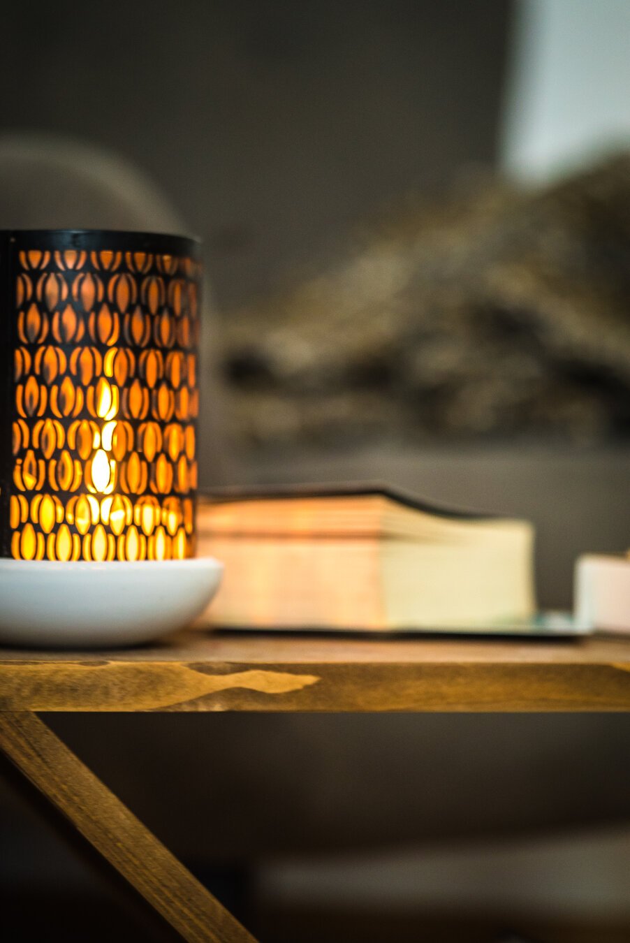 A side table with a burning candle, a book and a chair in the background