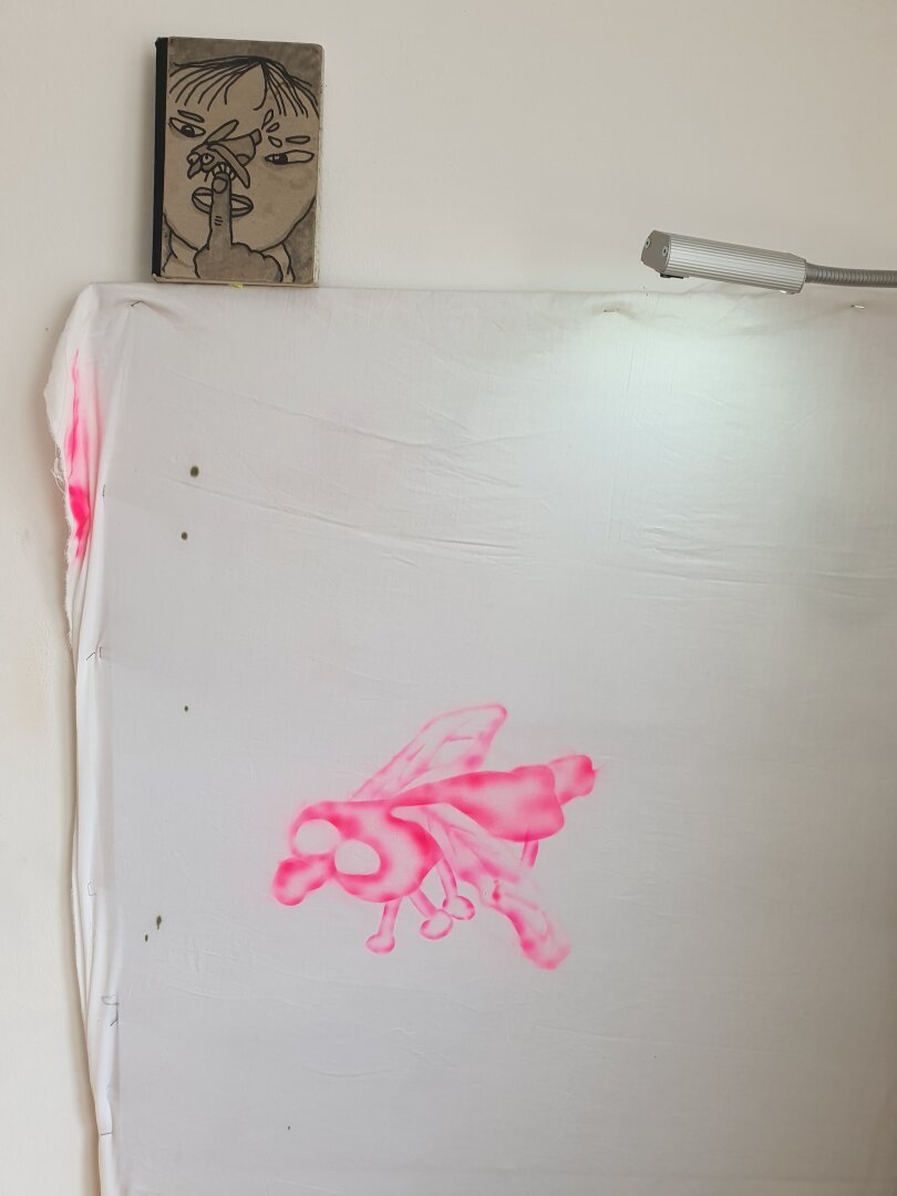 First stage of an airbrush painting, a pink fly painted on a white bedsheet.