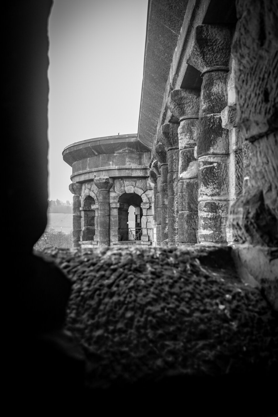 A photograph of the fascade of Porta Nigra in black and white. The photo is taken through one of its windows and shows the upper part of one of its apses