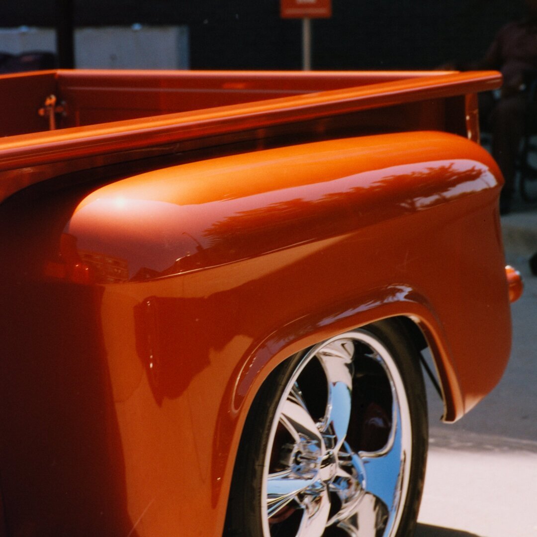 Rear quarter of an antique truck. The truck is painted a rusty orange and has modern rims.