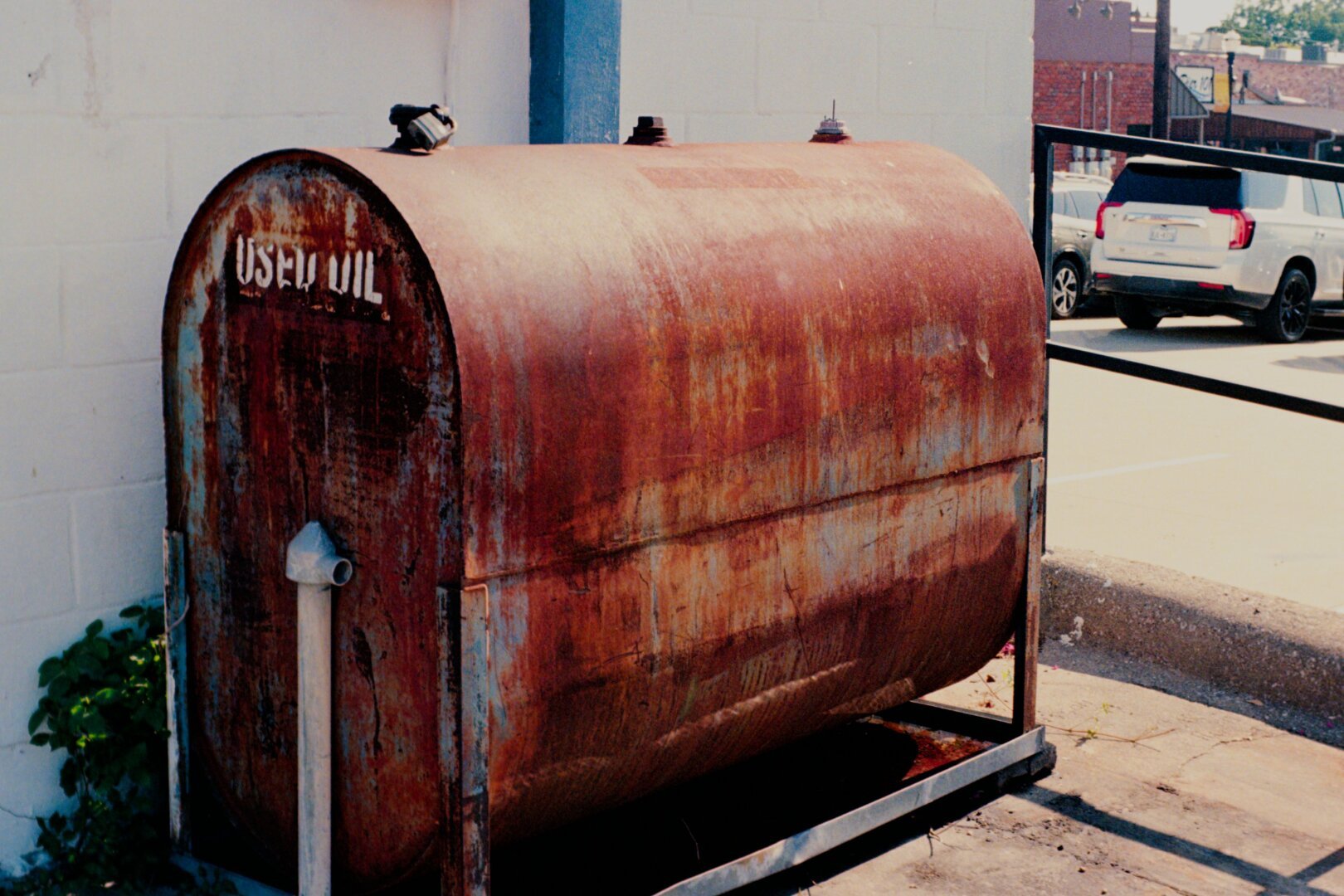 Used oil tank outside of a mechanic shop. It's oblong and a rusty orange color.