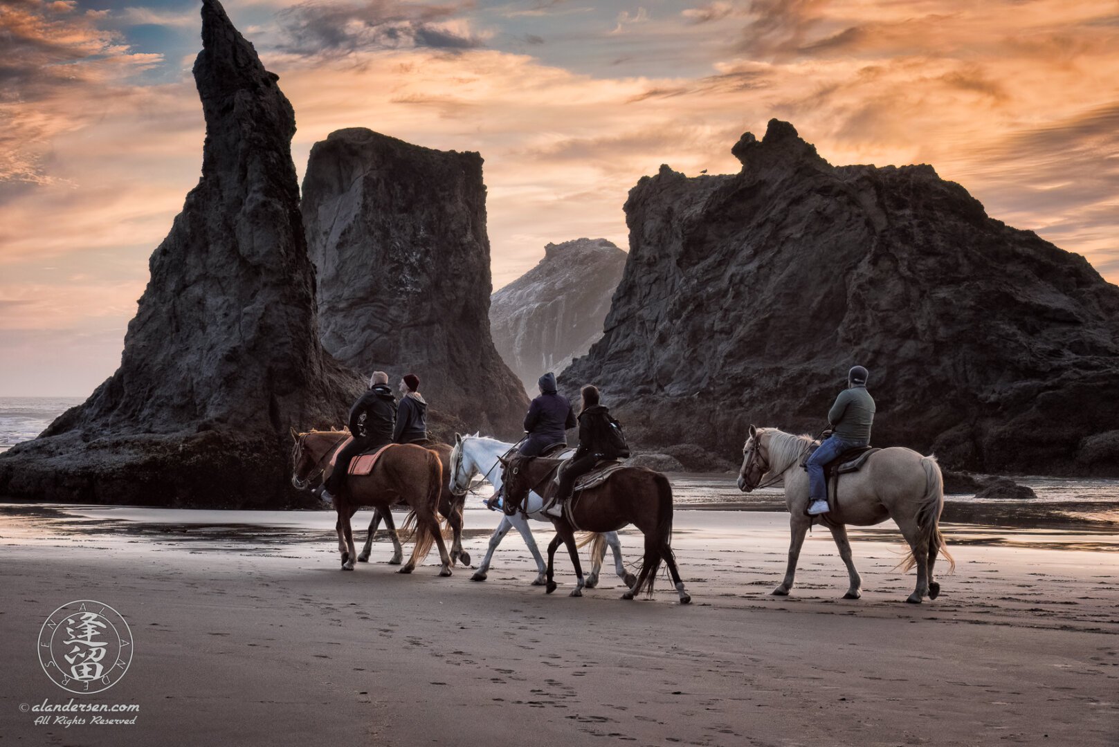 5 horseback riders on the sandy beach at Bandon, in Oregon, during low tide, admiring the other-worldly seastacks during an amazing sunset.