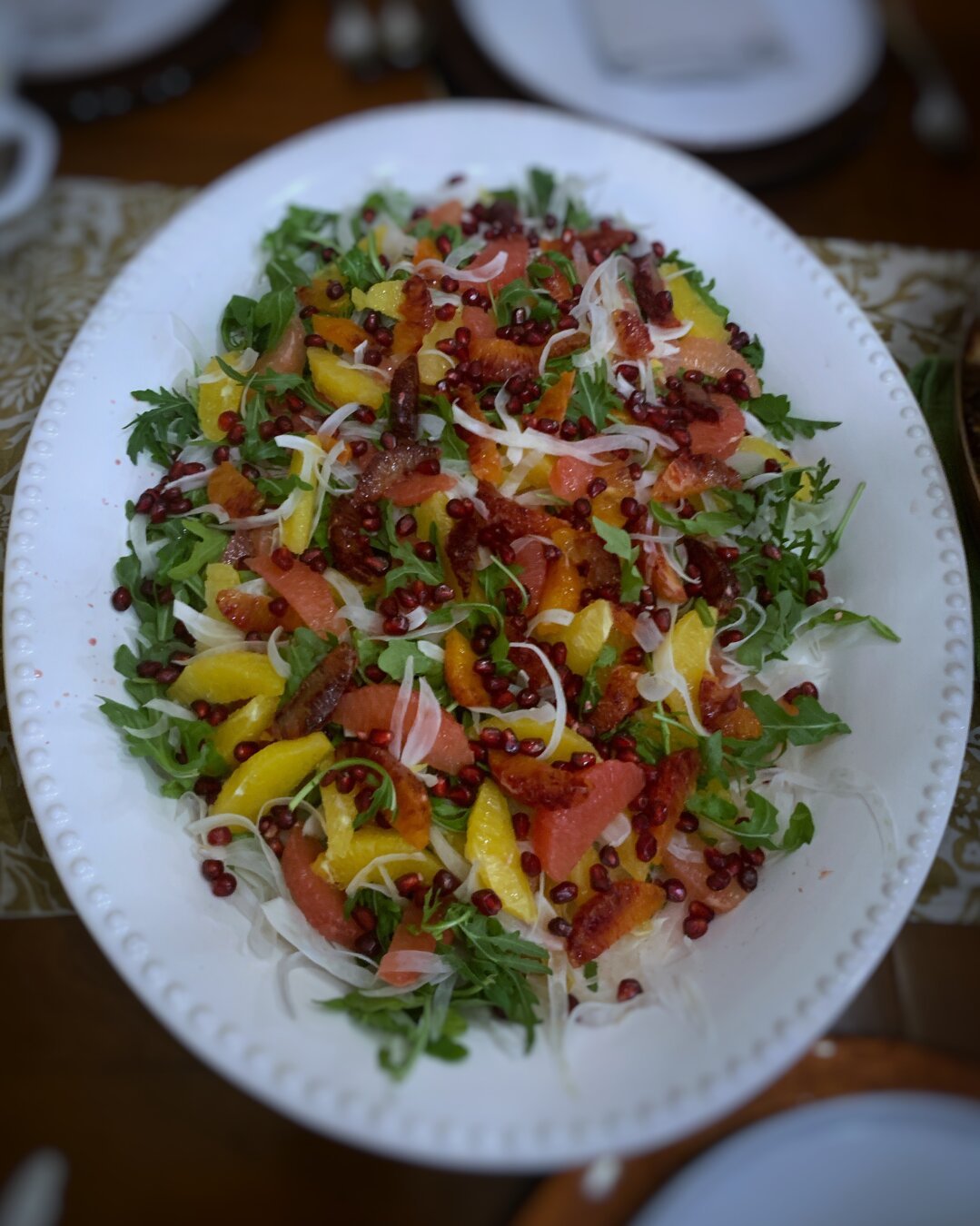 Colorful salad on a large, white platter with arugula, small citrus slices, and pomegranate seeds.