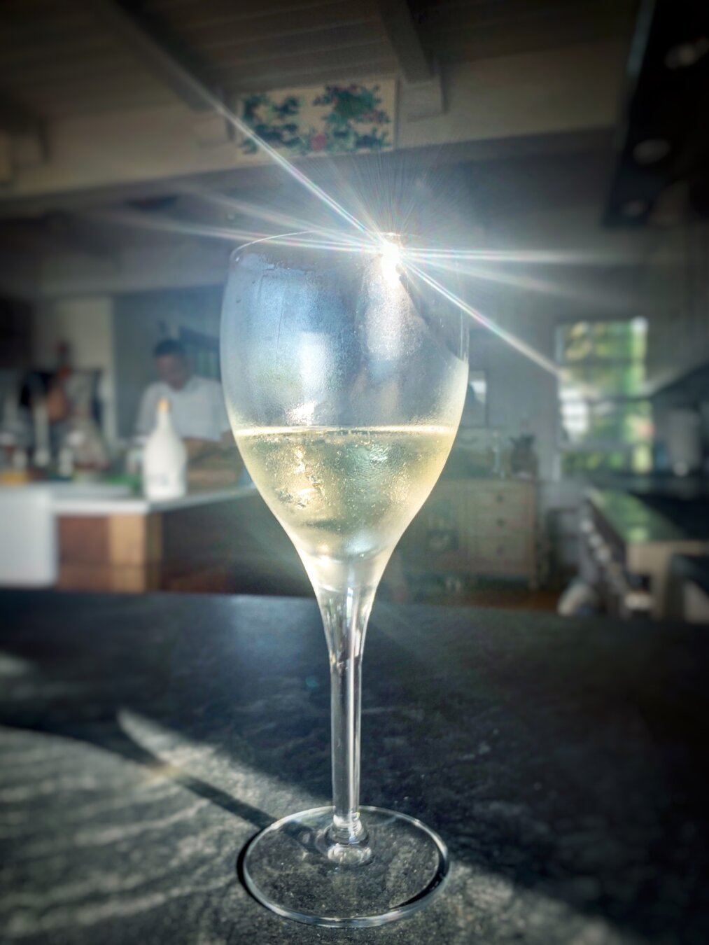 Glass of sparkling wine on a counter with light reflecting off it in a starburst pattern.