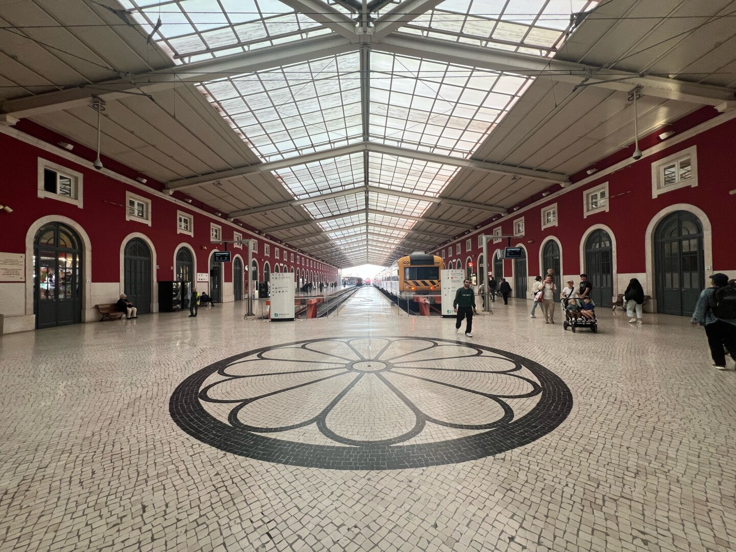 Train station with red walls and white ceiling from the inside. Two trains can be seen. The floor is a mosaic in black and white.