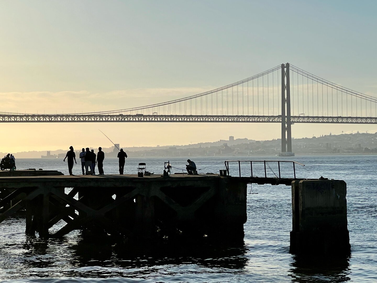 View of a suspension bridge with silhouettes of people in front.