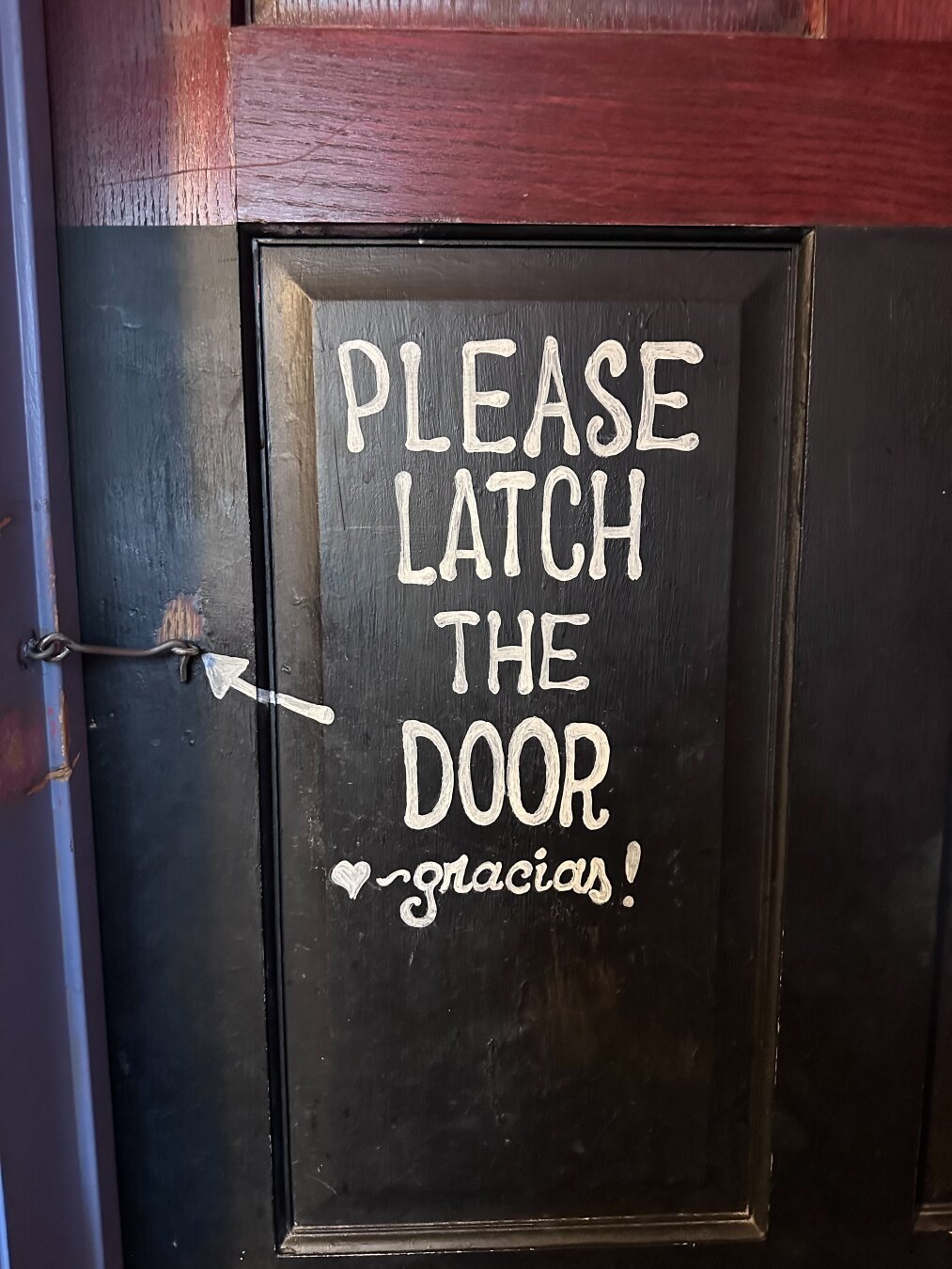 And old, reasonably well-kept, wooden door with the words “please latch the door, Gracias” painted on the inside in white letters