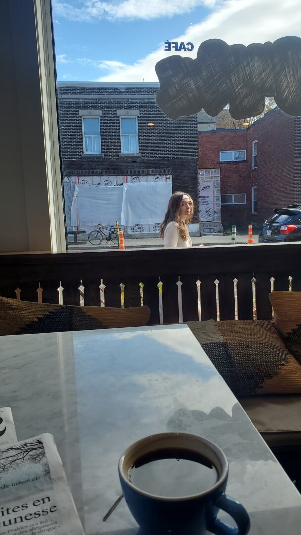 Montreal. Café table with newspaper and black coffee, facing a window on a sunny autumn adternoon. On the street, a person looks in the wi dow as she passes.