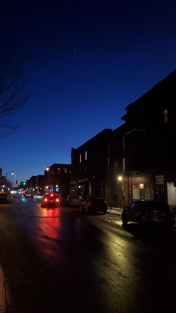 Peaceful street scene at dusk in Montreal's Mile End neighbourhood. Venus is rising and the sky is a deep blue, with the wet streets reflecting lights from homes, streetlights, and cars