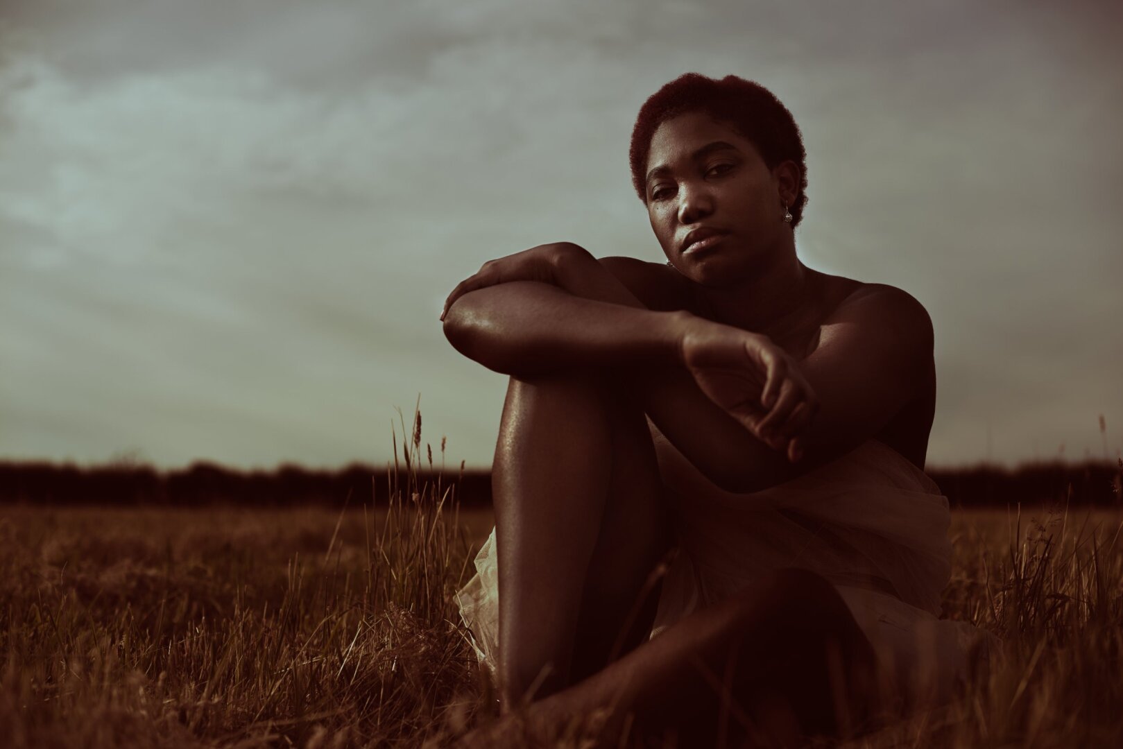 Stylised photo of woman sitting in a field, looking directly to camera