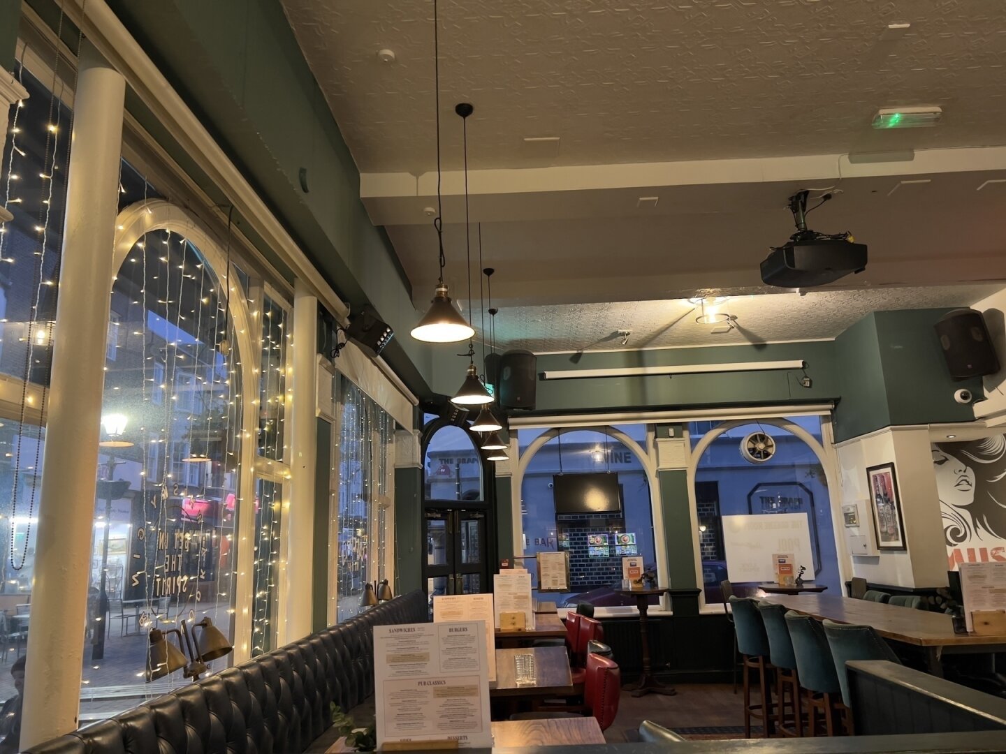 A cozy pub interior features string lights, arched windows, and a mix of tables and booths.