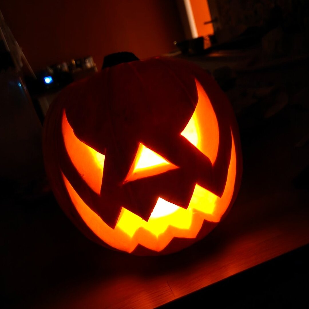 A spooky carved pumpkin lit from inside in a dark kitchen