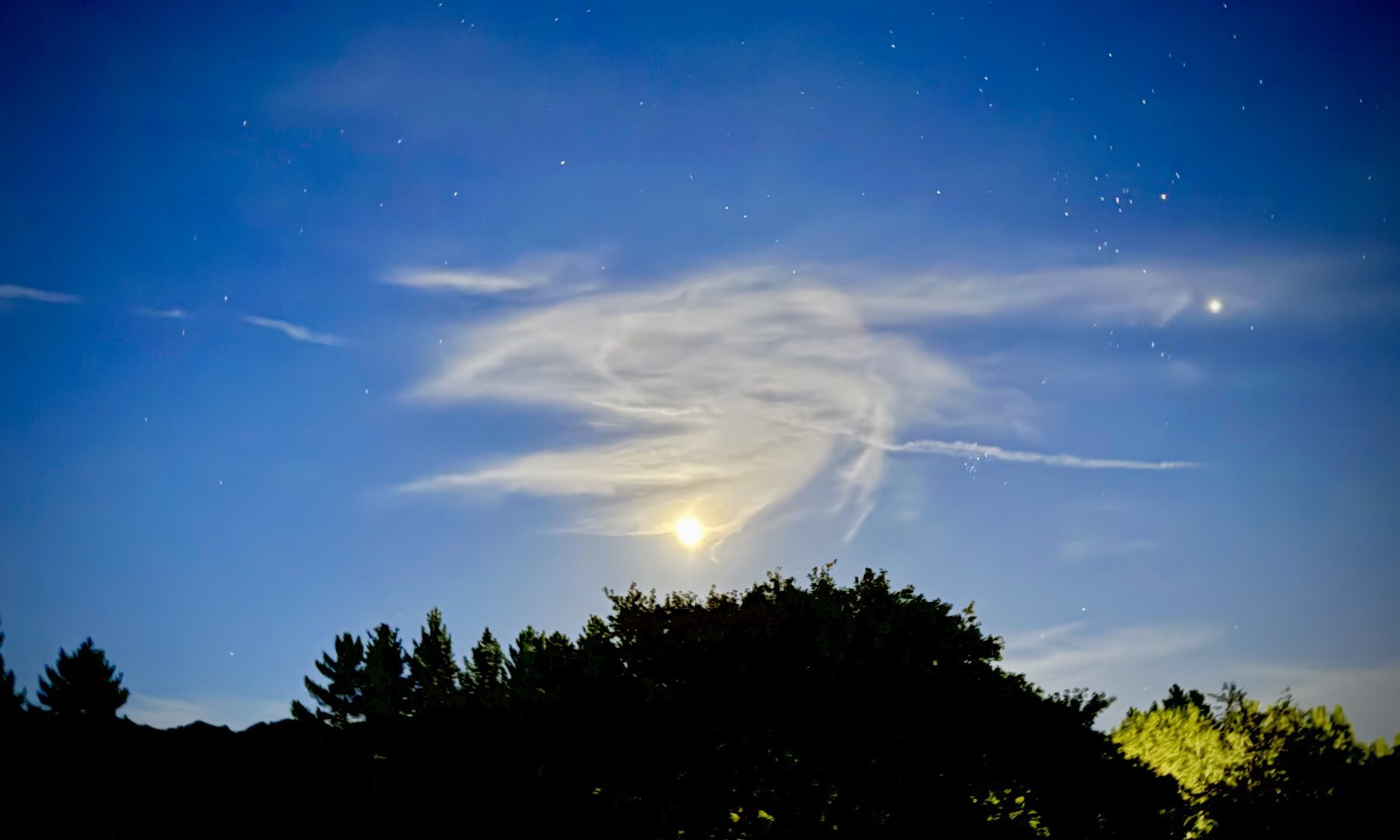 A cloud over the moon, with a swirly shape. To the right, Jupiter. Below, a tree line