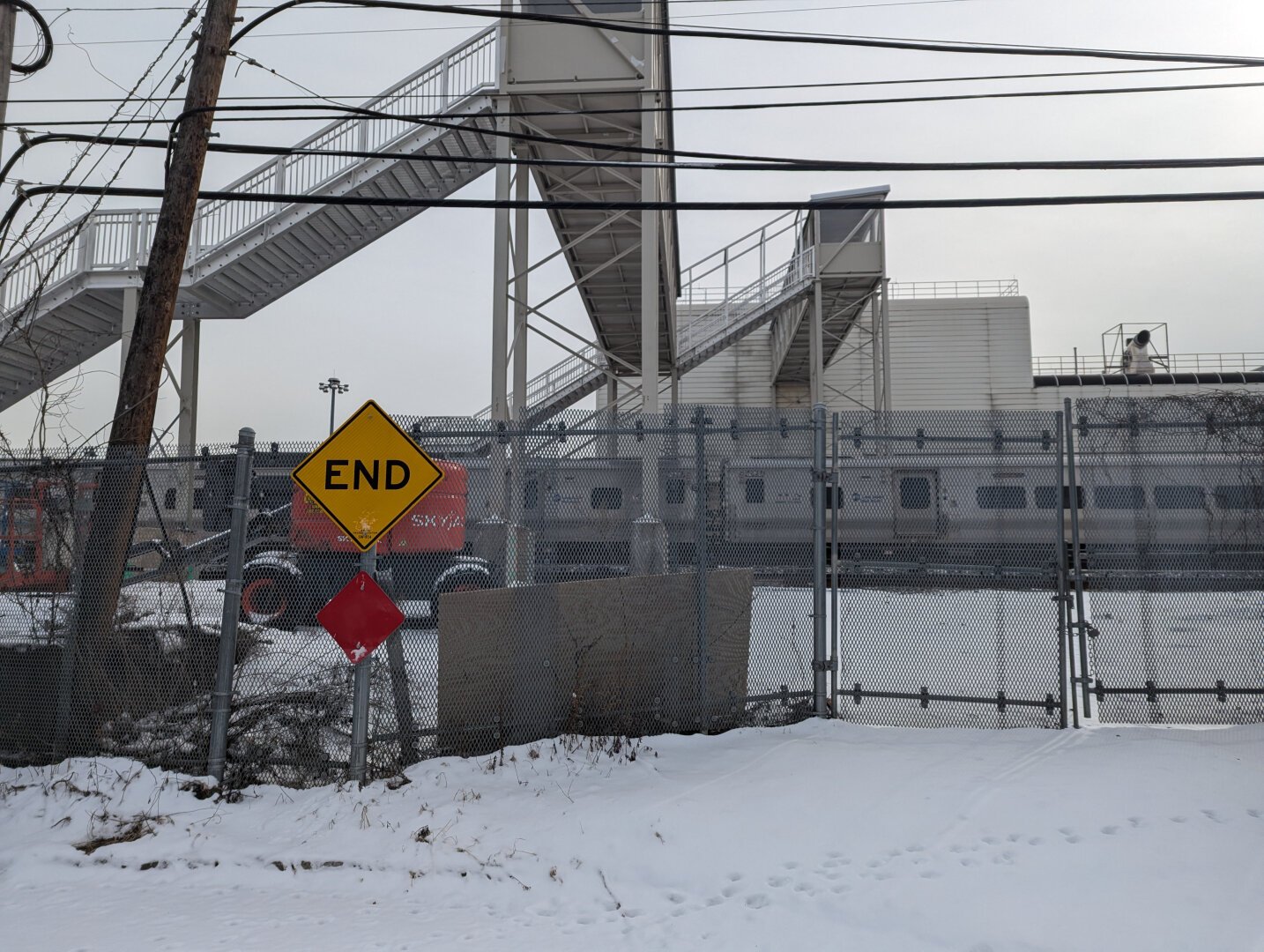 Gate, elevated staircases, pedestrian skyway, END sign, train passing in past below pedestrian skyway.