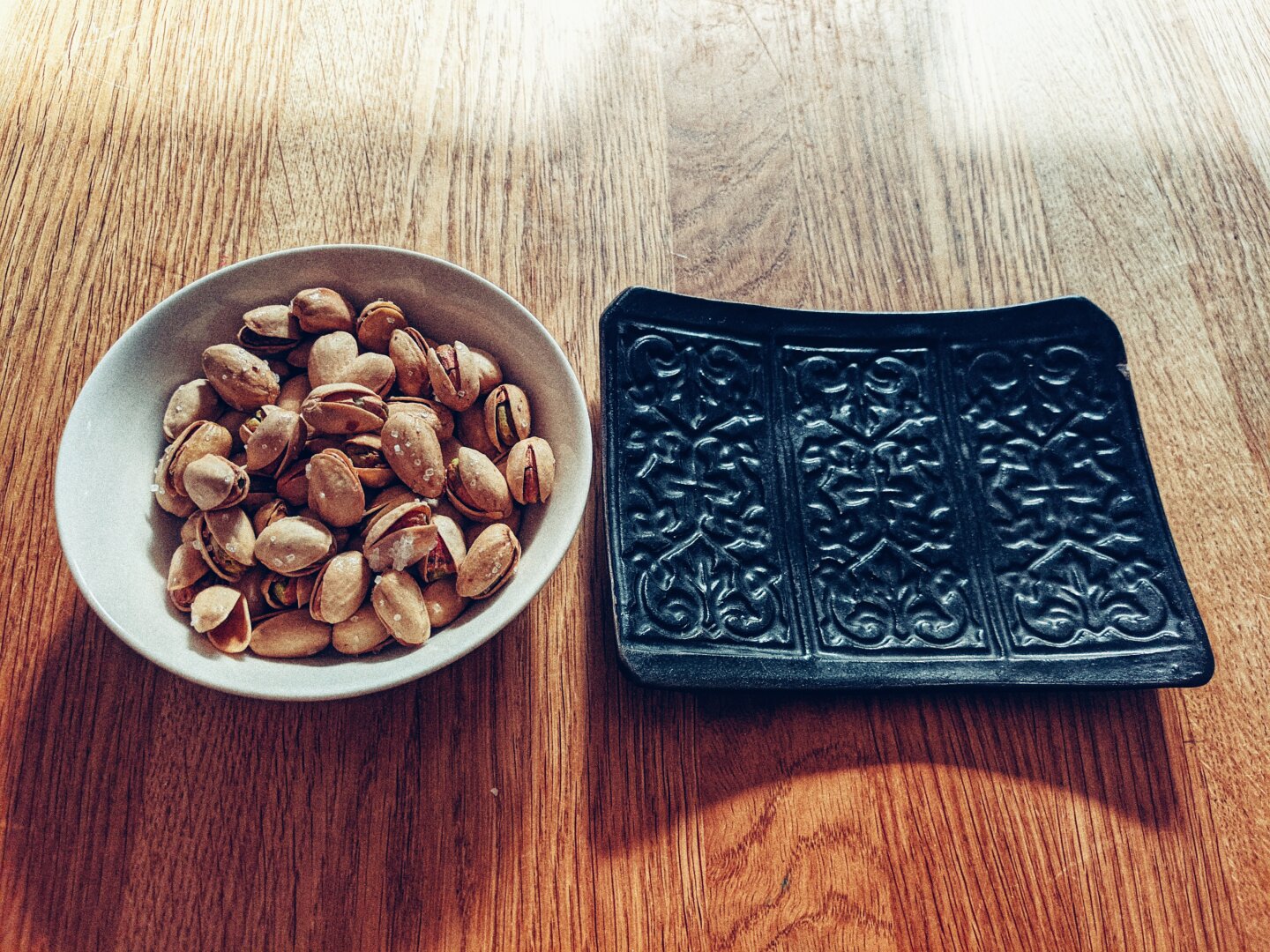 Pistachios in a small white dish and a black rectangular tile for the shells on the right